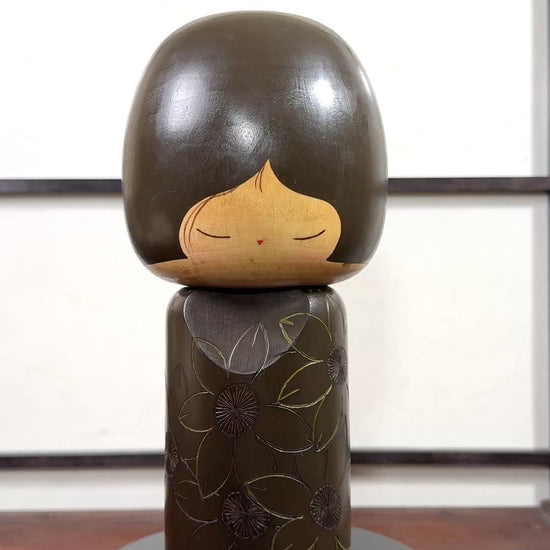 Kokeshi vintage de Yuji Kawase datée de 1980, caractérisée par une grande tête brune, un corps étroit et un décor de fleurs gravées, la vidéo