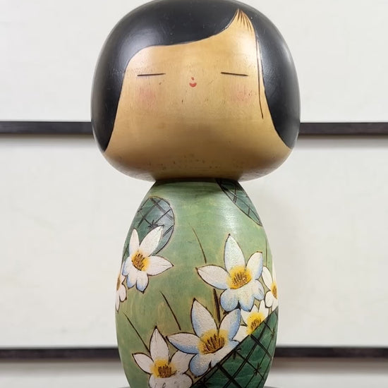 Kokeshi vintage de Yuji Kawase datée de 1994, au corps vert décoré de fleurs blanches et à la coiffure noire asymétrique, la vidéo à 360 degrés