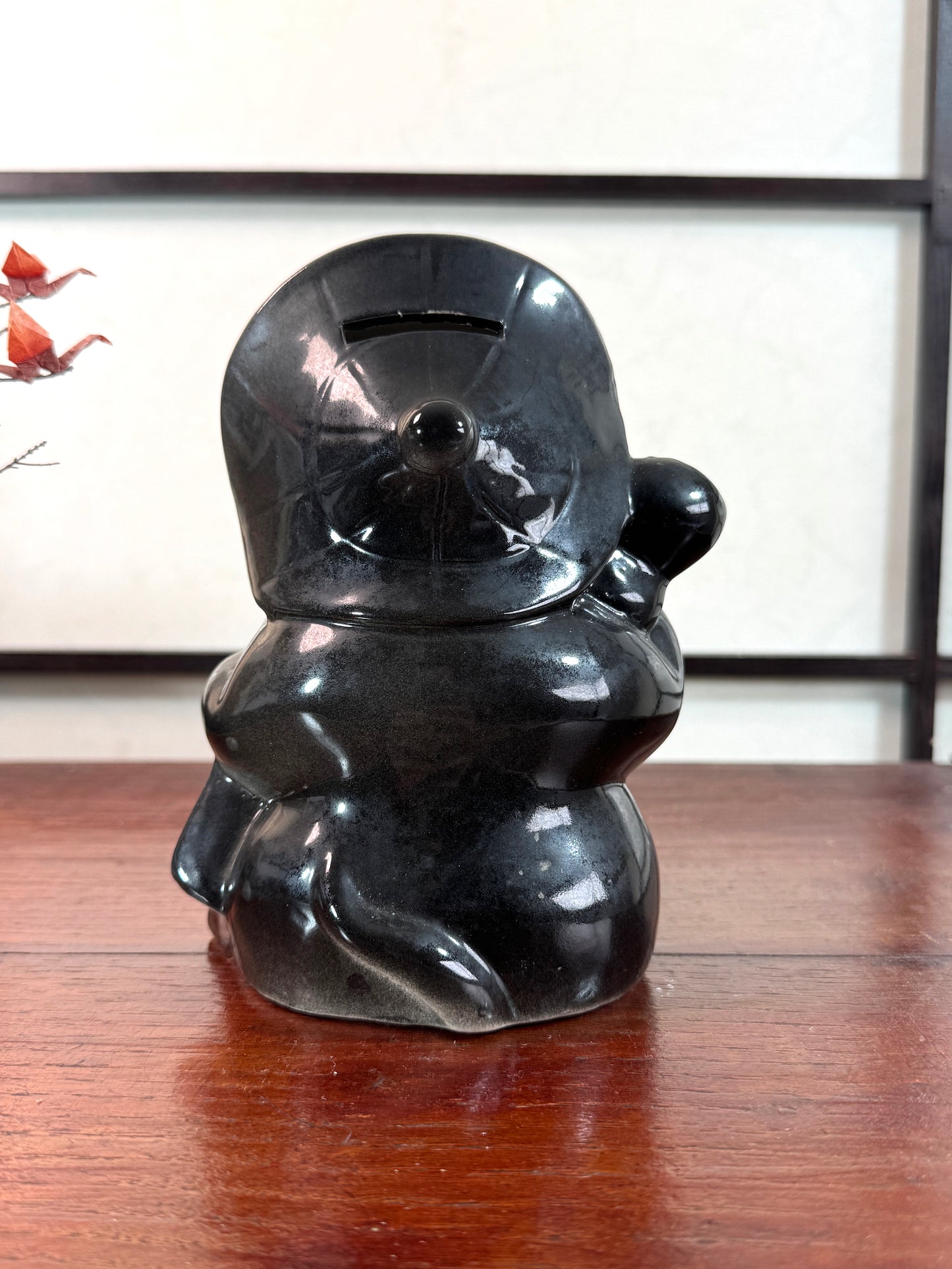 Tirelire tanuki en céramique émaillée noire et crème, style japonais traditionnel, vu de dos