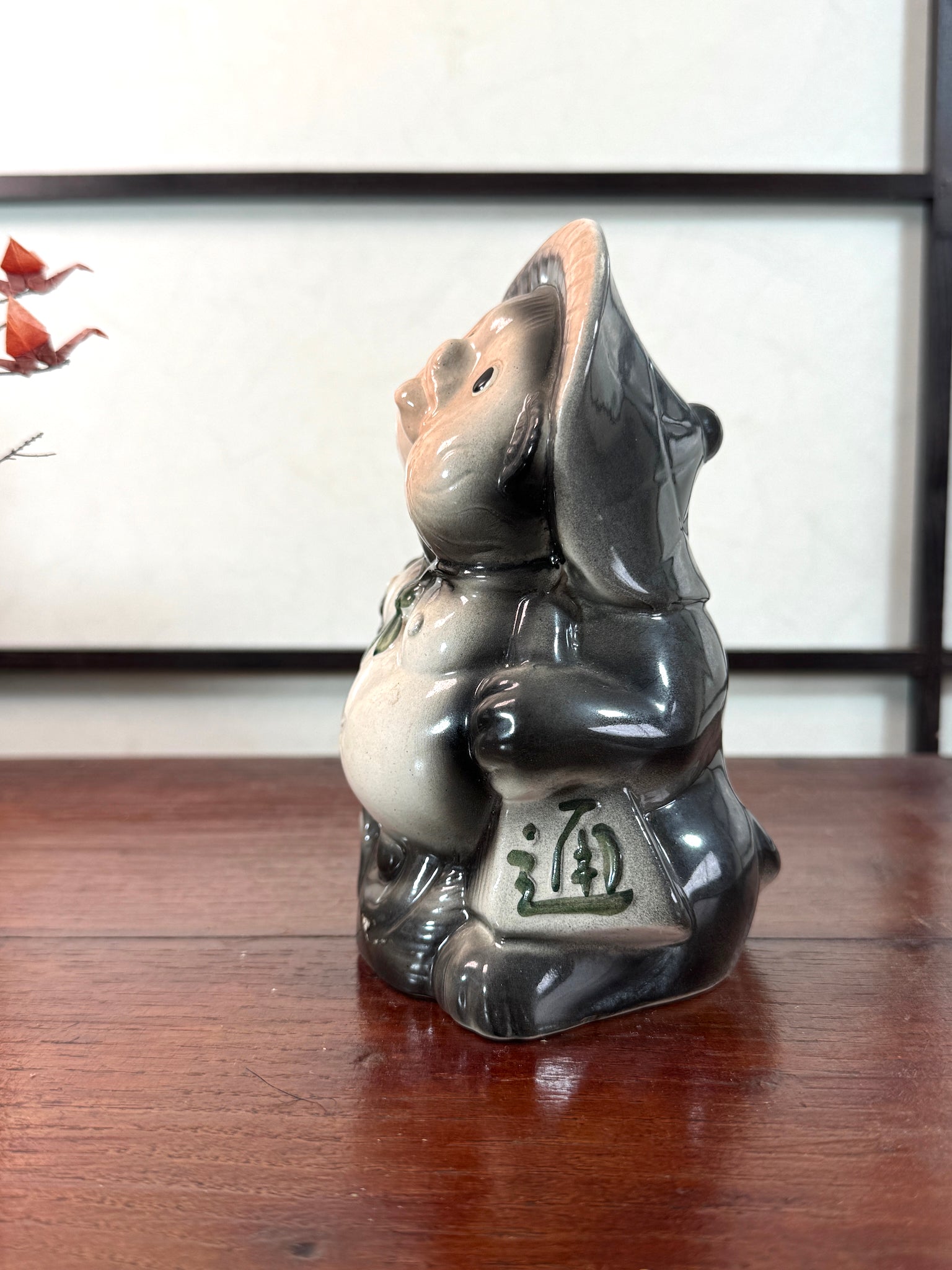 Tirelire tanuki en céramique émaillée noire et crème, style japonais traditionnel, vu du profil gauche