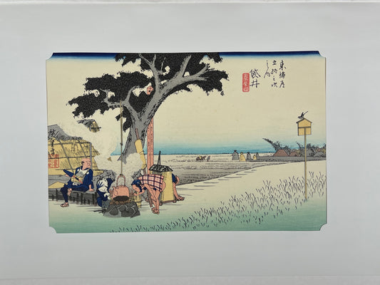 estampe japonaise de paysage d'Hiroshige, un homme et une femme attise le feu sous une bouilloire accrochée à un arbre au milieu des champs de riz, avec passe-partout d'origine