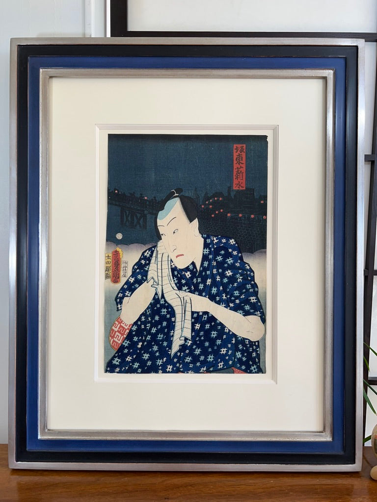 estampe japonaise ancienne de Kunisada d'un acteur de Kabuki sortant du bain et essuyant son visage sur fond de paysage nocturne urbain, encadré avec un cadre escalier noir, bleu et argent