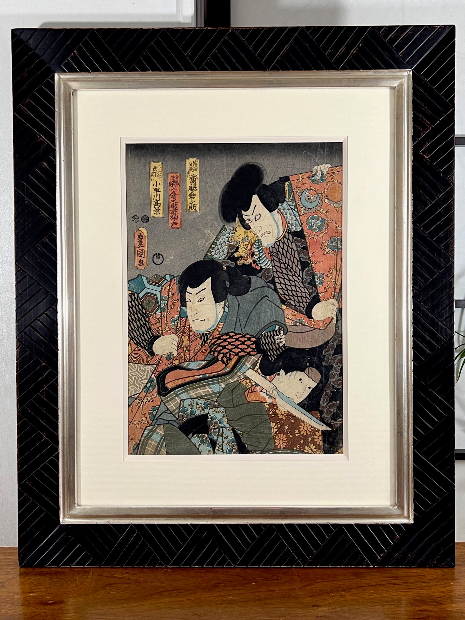 estampe japonaise originale de Kunisada représentant deus samouraïs dans une pièce de théâtre kabuki, encadrée avec un cadre noir strié et or blanc