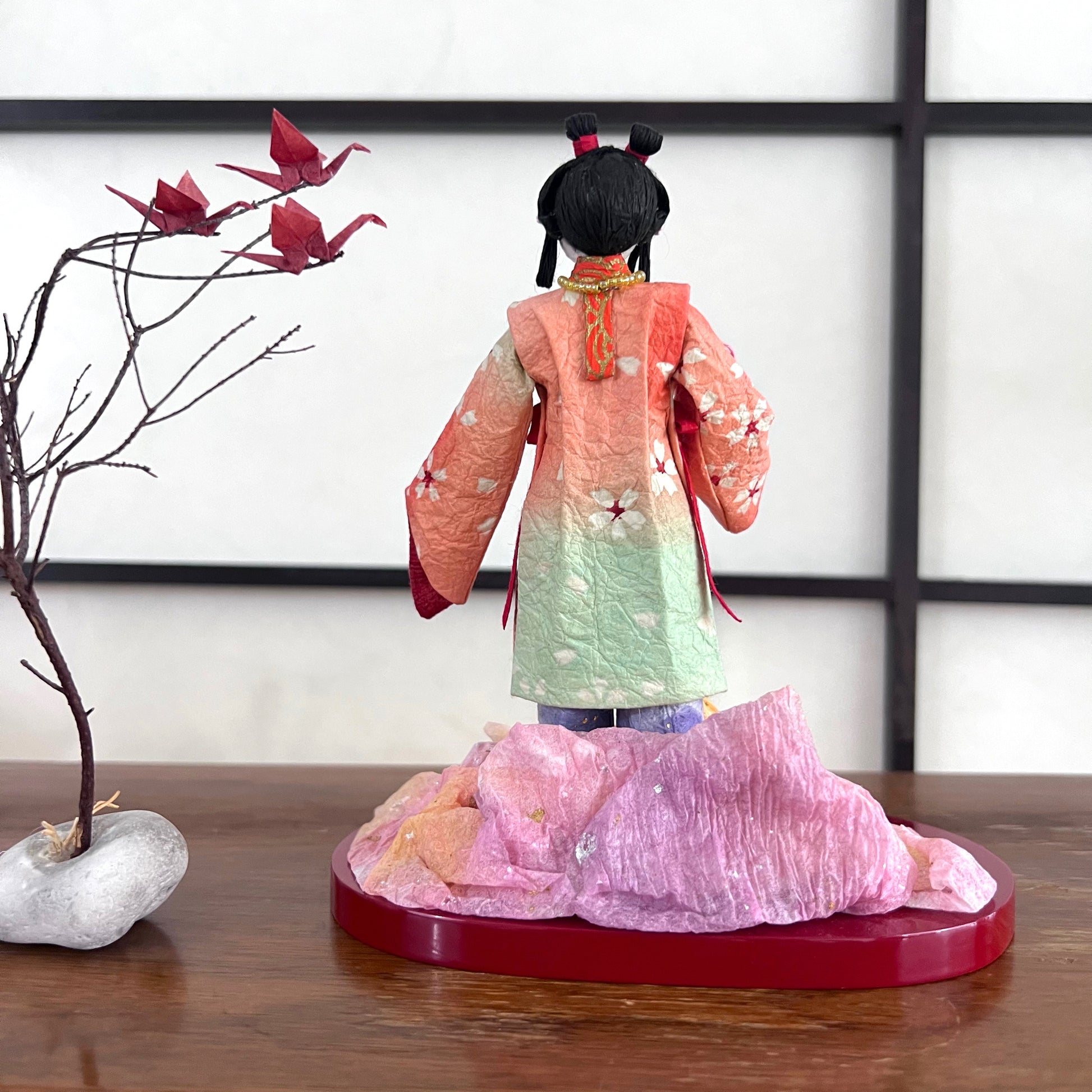 poupée japonaise en papier Yuzen Washi, ( Washi Doll)au kimono fleurs de cerisier tenant une pivoine rose dans la main, vu de dos