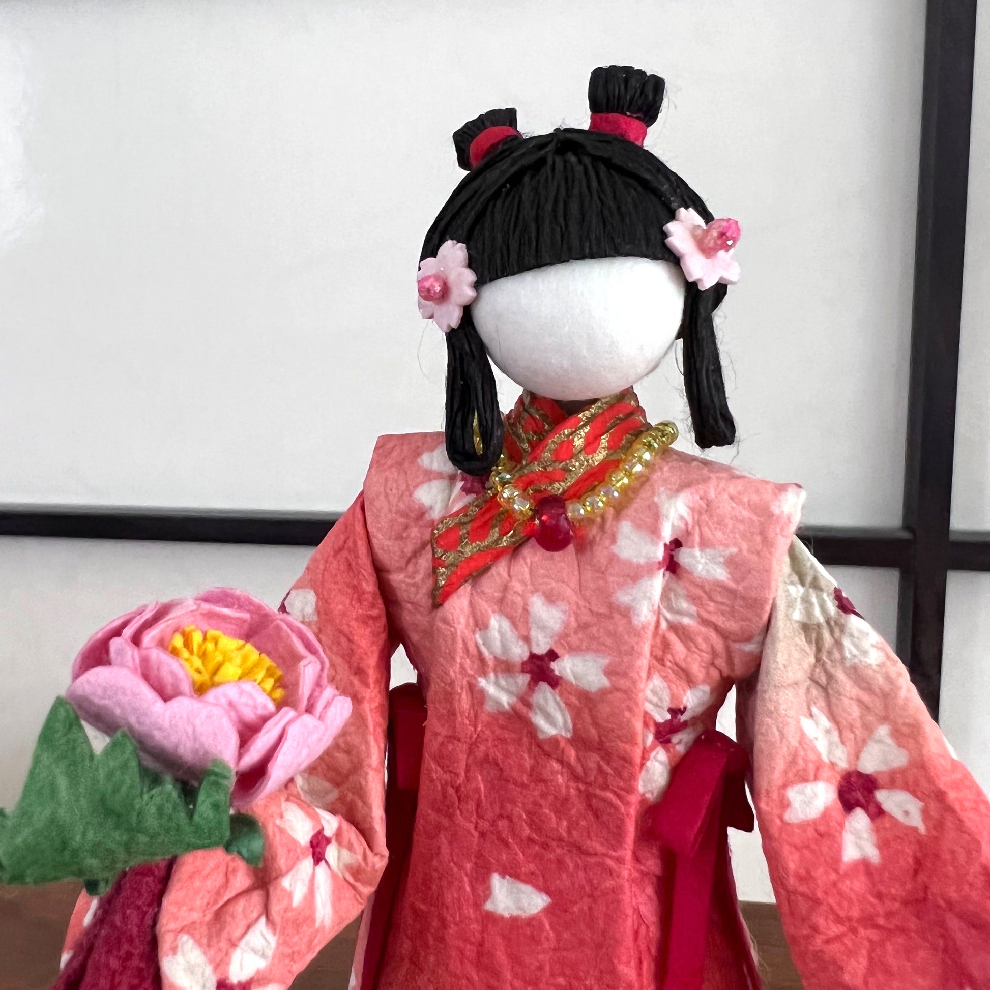 poupée japonaise en papier Yuzen Washi, ( Washi Doll)au kimono fleurs de cerisier tenant une pivoine rose dans la main, gros plan du visage 